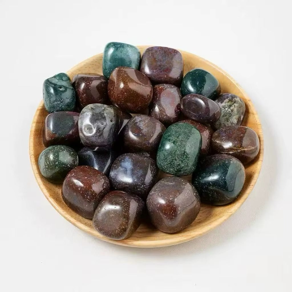 Overhead view of approximately 22 polished bloodstone and mixed jasper tumbles in a small wooden bowl, showing deep green, burgundy, and dark teal coloring with waxy gloss finish