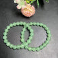 Two green aventurine 8mm bead stretch bracelets overlapping on dark leather surface with pink flower prop, top-down view showing soft apple-green color and vitreous luster