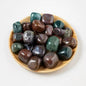 Overhead view of approximately 22 polished bloodstone and mixed jasper tumbles in a small wooden bowl, showing deep green, burgundy, and dark teal coloring with waxy gloss finish