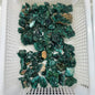 Overhead view of a white plastic bin filled with dozens of raw and druzy Dioptase cluster specimens from Congo, showing deep emerald-green vitreous crystals on matrix, thumbnail to small cabinet size.