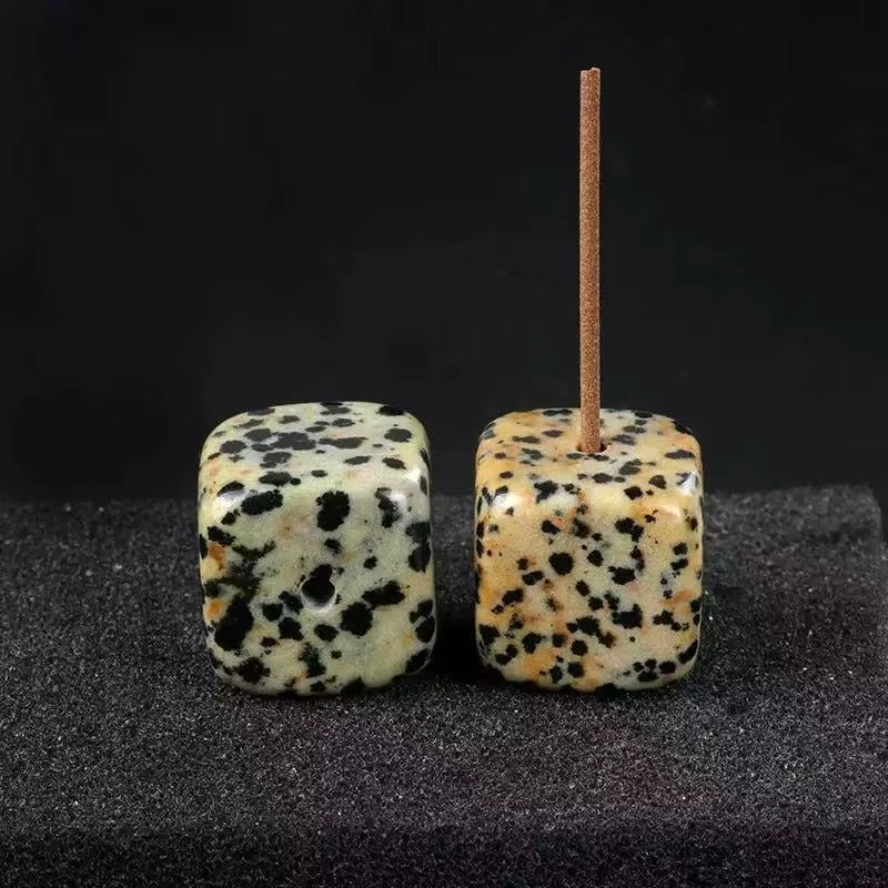 Two polished Dalmatian Jasper 20mm cube incense holders side by side on dark fabric, showing cream base with bold black spots; right cube has incense stick inserted