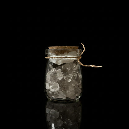 Zebra Industries, LLC corked glass jar filled with clear quartz tumbled mineral chips on a black background.
