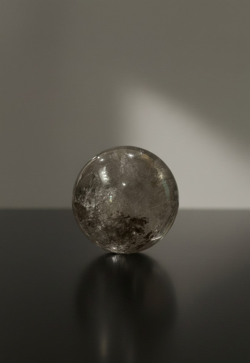 Zebra Industries, LLC collector grade polished garden quartz sphere with natural inclusions on a dark reflective surface.