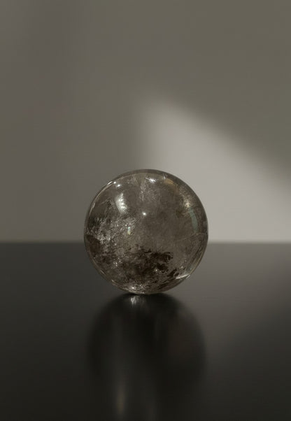 Zebra Industries, LLC collector grade polished garden quartz sphere with natural inclusions on a dark reflective surface.