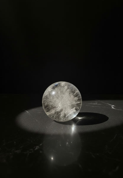 Zebra Industries, LLC polished 2-inch garden quartz sphere with wispy internal inclusions on a dark marble surface.