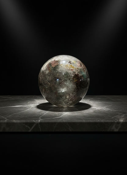 Zebra Industries, LLC garden quartz sphere with green chlorite inclusions and phantom formations on a marble surface.