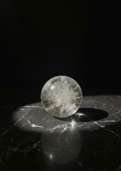 Zebra Industries, LLC 2-inch polished garden quartz sphere with internal inclusions on a black marble surface.